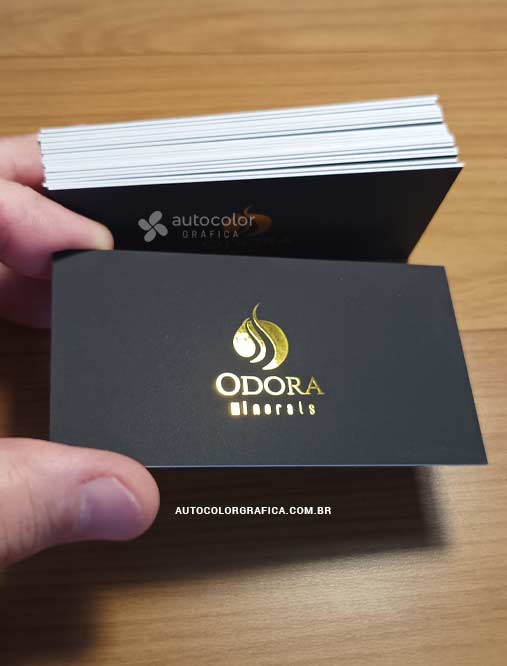 Cartão preto com logotipo em foil dourado diante de uma pilha de cartões